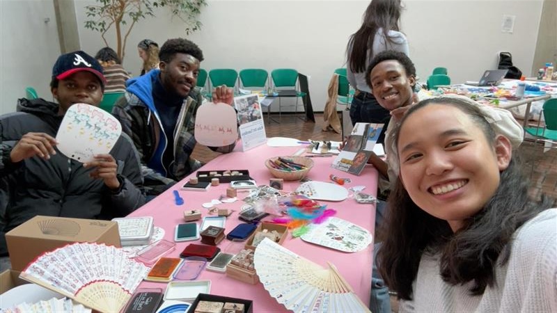 Students making paper fans at a pink table.